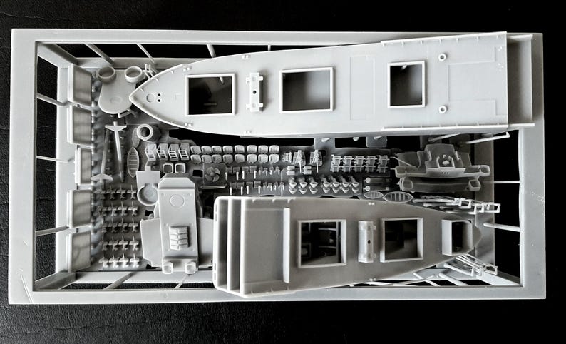 Peut inclure: Un cadre de kit de mod&eacute;lisme en plastique gris contenant deux coques de navires non peintes et divers petits composants. La grappe comprend de multiples pi&egrave;ces miniatures, dont des petites chaises, des &eacute;l&eacute;ments structurels et des accessoires de pont.