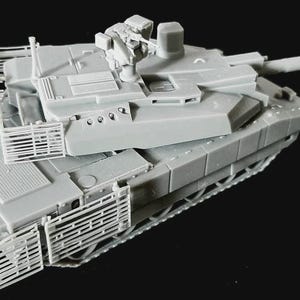 Op de afbeelding: Een lichtgrijs schaalmodel van een gevechtstank met een lange loop, een draaibare koepel met een gemonteerd machinegeweer en beschermende lattenpantserkooien rondom de zijkanten van de romp en de koepel, alles uitgevoerd in een matte afwerking.