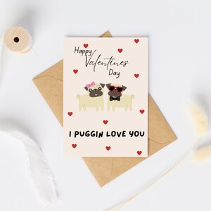 May include: Valentine's Day card with two cartoon pugs, one with a pink bow and the other with heart-shaped sunglasses and a bow tie. The card reads "Happy Valentine's Day" and "I Puggin Love You" with red heart accents.