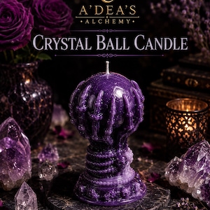 May include: A purple wax candle shaped like a crystal ball held by skeletal hands, resting on a base decorated with small skulls. The text A'DEA'S ALCHEMY and CRYSTAL BALL CANDLE is printed above the candle in white and gold lettering.
