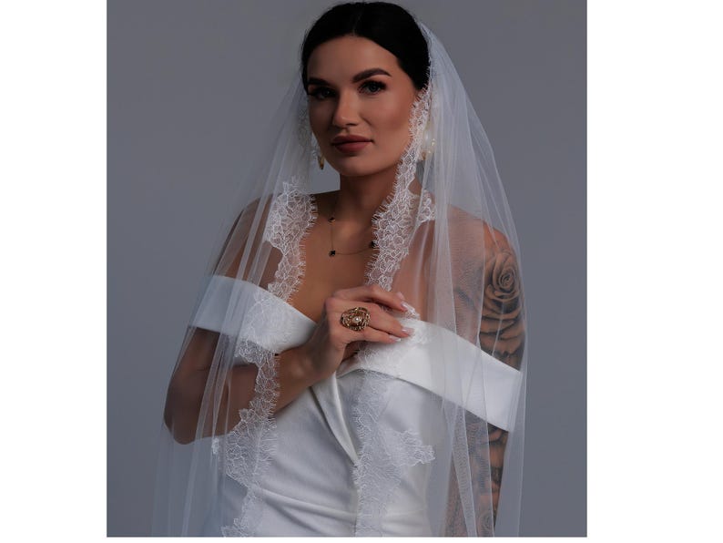 Bride wearing ivory wedding veil gathered at comb with Chantilly lace edge and long flowing train