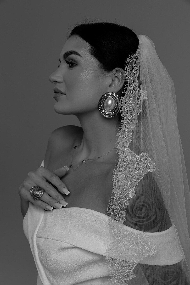 Bride wearing ivory wedding veil gathered at comb with Chantilly lace edge and long flowing train