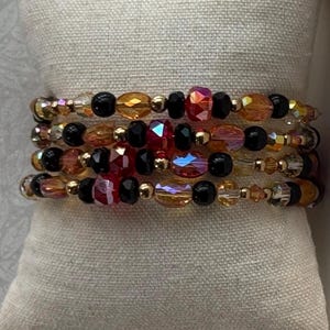 Peut inclure: Un bracelet multi-rangs composé d'un motif répétitif de perles à facettes dans des tons rouge, ambre et cristal transparent, alternées avec de petites perles noires rondes et de minuscules perles intercalaires dorées.
