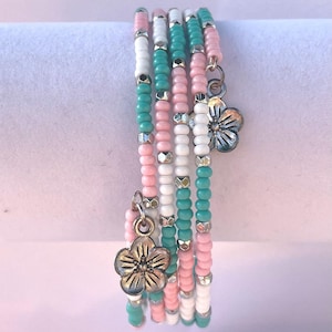 May include: Set of six beaded bracelets with flower charms. The bracelets are pink, white, and turquoise.