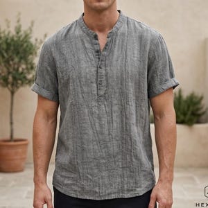 May include: A gray short-sleeve shirt with a mandarin collar and a button-down placket. The shirt has a textured appearance and rolled-up sleeves. The image also shows the logo for Hexaras Clothing Shop.