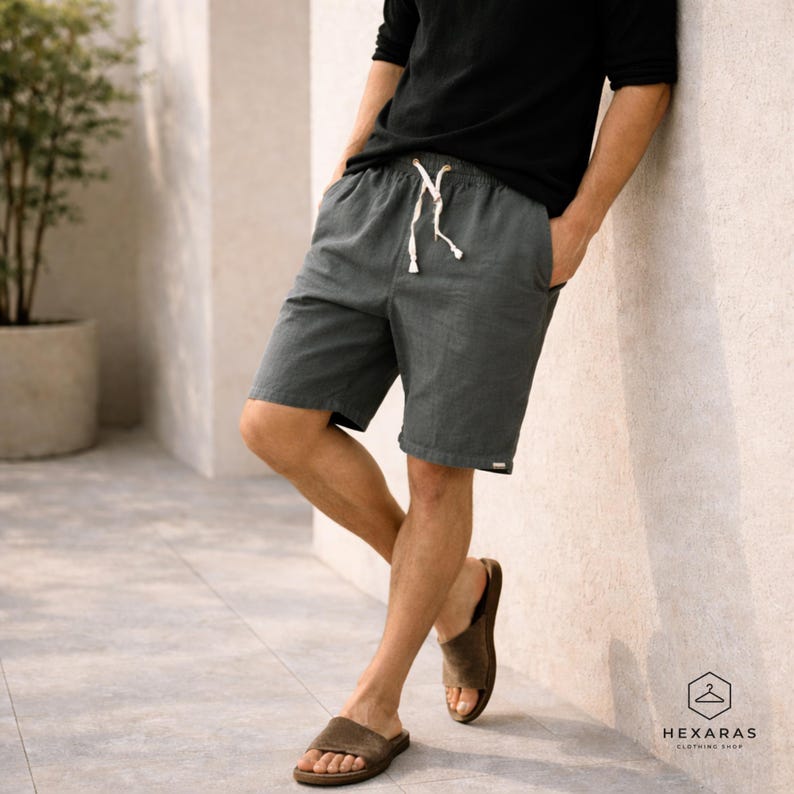 May include: Charcoal gray shorts with a drawstring waist and side pockets. The shorts are paired with brown sandals. The person is wearing a black long-sleeve shirt. The image is taken outdoors.