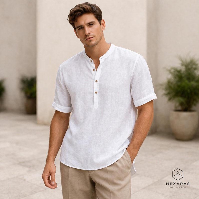 May include: A white linen shirt with a mandarin collar and short sleeves. The shirt has a button-down placket with three wooden buttons. The model is wearing khaki-colored pants. The shirt is from Hexaras Clothing Shop.