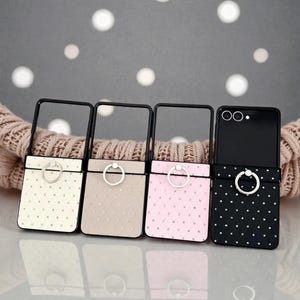 Op de afbeelding: Vier telefoonhoesjes in crème, beige, roze en zwart, elk met een ringhouder en een gewatteerd patroon. De hoesjes hebben een zwart frame en een ringhouder. De zwarte hoes heeft een stippenpatroon.