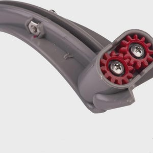 Op de afbeelding: Een grijs plastic onderdeel met twee rode tandwielen en zilveren schroeven. Het gebogen stuk heeft een afgerond uiteinde en een rechthoekige behuizing voor de tandwielen. De tandwielen zijn zichtbaar in de behuizing.