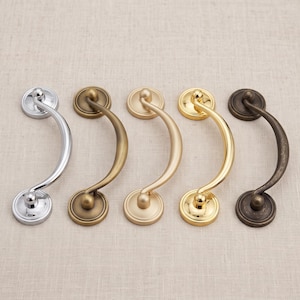 May include: Five curved metal drawer pulls arranged in a row. The finishes include polished chrome, antique brass, matte gold, polished gold, and oil-rubbed bronze. Each handle features a central arched bar attached to two circular mounting plates.