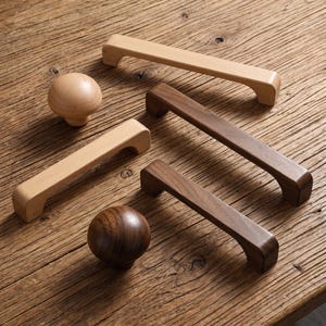 May include: A collection of wooden cabinet hardware including two spherical knobs and three rectangular drawer pulls. The set features two distinct wood tones, with one light-coloured wood and one dark-coloured wood, each showing a smooth finish.