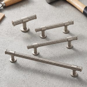 May include: Four silver-toned metal cabinet pulls of varying lengths, each featuring a textured, woven-style pattern along the cylindrical handle and supported by two circular mounting bases, except for the smallest pull which has one base.