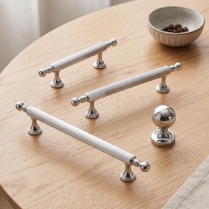 Peut inclure: Trois poignées de tiroir en métal argenté au design cylindrique cannelé avec des embouts sphériques, accompagnées d'un bouton de meuble sphérique assorti. Chaque pièce présente une finition polie et une base solide pour la fixation.