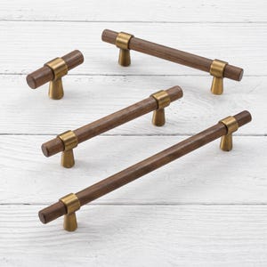 May include: A collection of four cabinet pulls and a knob featuring cylindrical dark brown wood bars accented with brushed brass metal mounts. The hardware set includes one small knob and three handles of varying lengths with metallic bases.