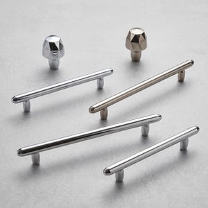 May include: A collection of cabinet hardware including two faceted, geometric knobs and four cylindrical bar pulls in polished chrome and brushed nickel finishes, featuring smooth, rounded ends and sturdy mounting posts for attachment.