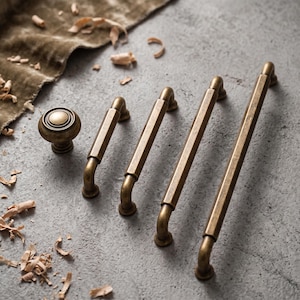 May include: A collection of antique brass hardware including one round cabinet knob and three linear drawer pulls of varying lengths. Each piece features a smooth, metallic finish with a slightly weathered, darkened patina and rounded mounting posts.