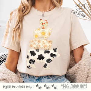 以下が含まれることがあります： ベージュのTシャツに、積み重ねられた動物のデザイン。デザインには、黒い斑点のある牛、花の豚、太陽のある羊、花のある鶏が含まれています。「Digital Download Only!」の文字が下にあります。