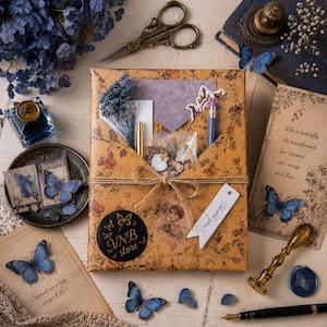 Peut inclure: Un paquet cadeau rectangulaire enveloppé dans du papier floral marron avec un nœud en ficelle, contenant des articles de papeterie, un encrier bleu, des ciseaux vintage, un sceau à cire, un stylo plume et des cartes avec des papillons et du texte.