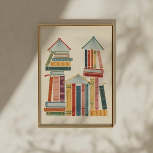 Puede incluir: Una lámina artística enmarcada que presenta una colección de libros dispuestos para formar tres estructuras en forma de casa. La ilustración utiliza una paleta de tonos apagados en rojo, azul, verde, amarillo y rosa, mostrando lomos de libros.