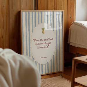 Op de afbeelding: Een ingelijste kunstprint met een lichtblauwe en witte verticaal gestreepte achtergrond. In het midden bevat een ovaal geschulpt kader de tekst "Even the smallest one can change the world." met een kleine illustratie van wortels erboven.