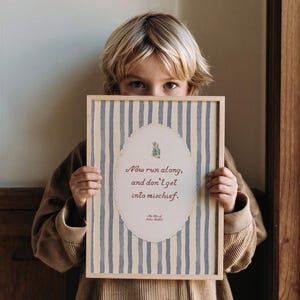 May include: A rectangular framed print featuring a light blue and cream vertical striped background. In the center, an oval scalloped border surrounds a small illustration of a rabbit and the text: Now run along, and don't get into mischief.