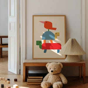 Puede incluir: Una lámina de arte enmarcada con una ilustración apilada de un pájaro rojo, una tortuga azul y una tortuga roja sobre un fondo crema. La obra se exhibe junto a una lámpara plisada beige y un oso de peluche de color marrón claro.