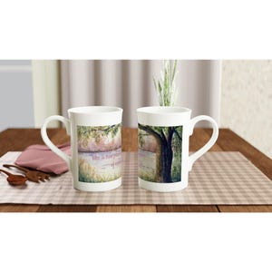 Peut inclure: Deux tasses en céramique blanche ornées d'une peinture aquarelle représentant un paysage avec un grand arbre près d'un point d'eau. Le motif inclut le texte 'like a tree planted by streams of water' écrit dans une police cursive douce au centre.