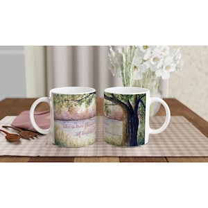 Peut inclure: Deux tasses en céramique blanche ornées d'une peinture aquarelle représentant un grand arbre au bord de l'eau. Le texte "like a tree planted by the waters..." est imprimé dans une police cursive sur le devant des tasses à anse courbée.