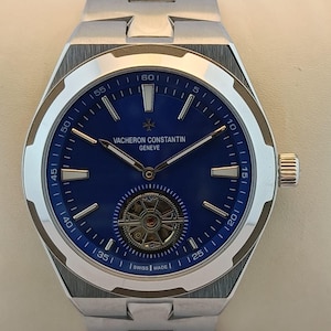 Peut inclure: Une montre Vacheron Constantin en acier inoxydable avec un cadran bleu. La montre présente une lunette argentée, des aiguilles argentées et un mouvement mécanique visible. Le bracelet de la montre est également en acier inoxydable. La montre est fabriquée en Suisse.