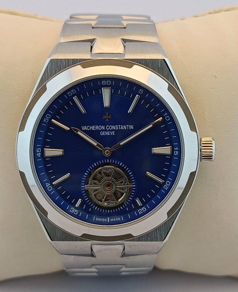 May include: A stainless steel Vacheron Constantin watch with a blue dial. The watch features a silver bezel, silver hands, and a visible mechanical movement. The watch band is also stainless steel. The watch is Swiss made.