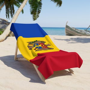 May include: A deckchair draped with the flag of Moldova, featuring blue, yellow, and red sections, and the Moldovan coat of arms. The chair is positioned on a sandy beach, with a boat visible in the background.