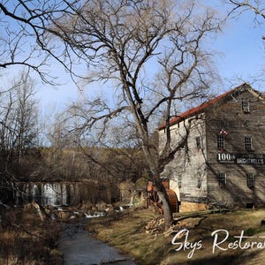 May include: An exterior shot of Brightwell's Mill, a historic wooden building with a red roof, set against a backdrop of trees and a flowing stream. The mill's water wheel is visible. The sky is blue.