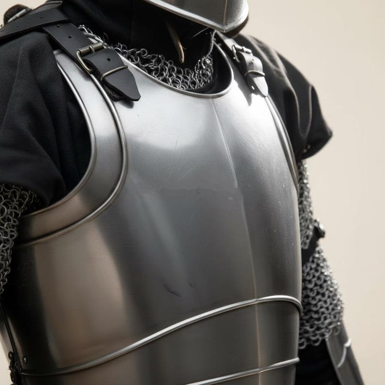 May include: Close-up of a polished steel breastplate with leather straps and buckles. The armor is part of a medieval knight's outfit, with chainmail visible on the side. The chest piece has curved edges and a reflective surface.