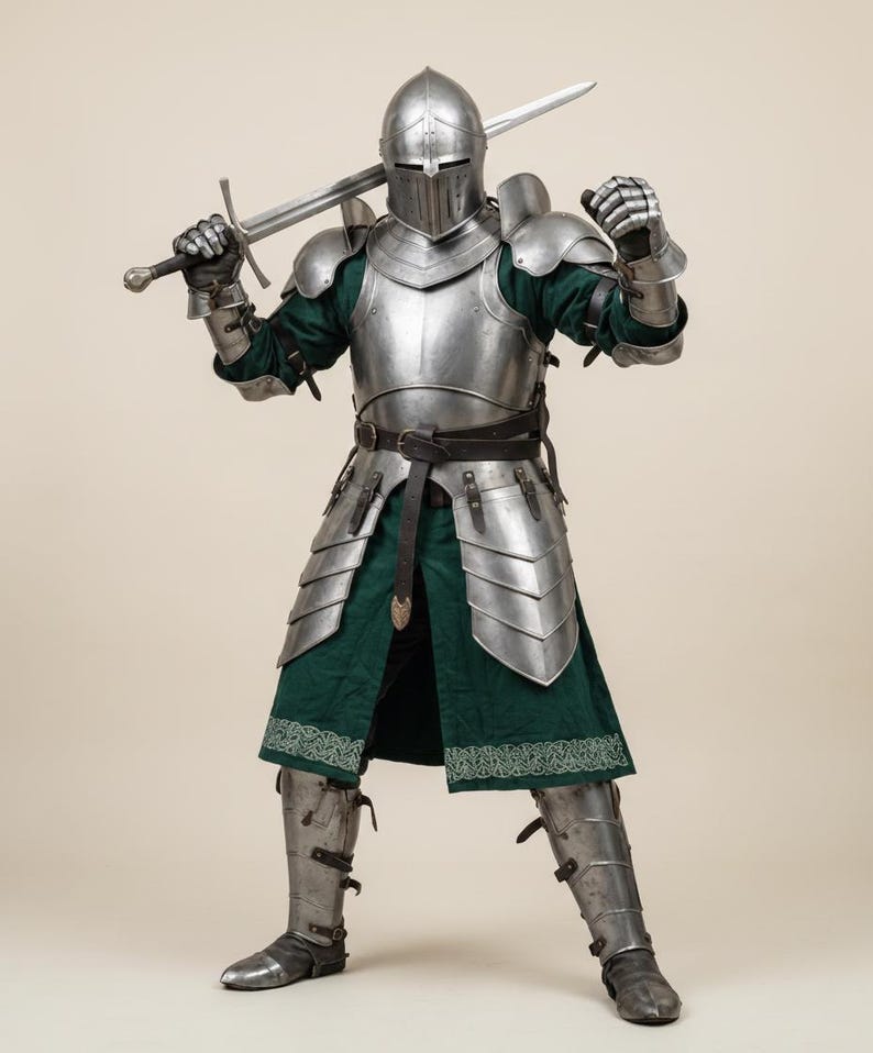 May include: A full suit of medieval armor, including a helmet, chest plate, and leg guards, is displayed. The armor is silver-colored and worn over a green tunic. A long sword is held over the shoulder. The armor is detailed and appears to be functional.