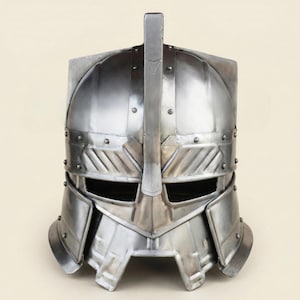 Peut inclure: Casque en métal argenté avec une crête verticale centrale et une construction rivetée. Le casque présente une visière et des éléments de design angulaires, évoquant un thème historique ou fantastique. Style médiéval ou viking.