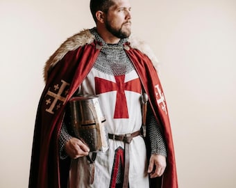 May include: A medieval-style costume featuring a white tunic with a red cross, a red cloak with faux fur trim and gold cross emblems, a metal chainmail coif, and a silver-toned metal helmet held in one hand with a brown leather belt.