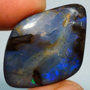 Könnte beinhalten: Ein polierter, unregelmäßig geformter schwarzer Opal-Edelstein mit einer dunklen Grundfarbe, lebhaften Blitzen in elektrischem Blau, tiefem Violett und subtilem grünem Schimmer, durchsetzt mit dunkelbraunen und schwarzen Matrix-Einschlüssen.