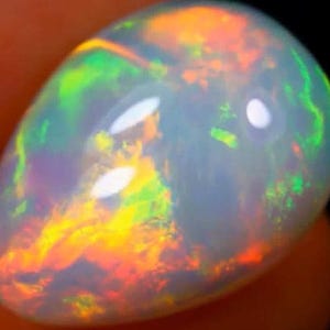 May include: A pear-shaped opal gemstone with a vibrant display of colors. The opal showcases a mix of orange, yellow, green, and blue hues, creating a shimmering effect. The stone has a polished, glossy surface, reflecting light.