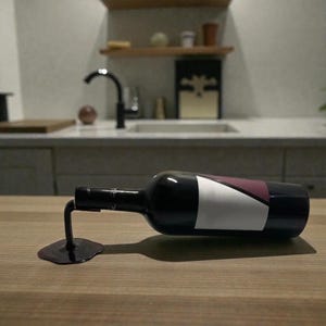 May include: A black wine bottle with a white and burgundy label, seemingly suspended in mid-air by a black metal stand that mimics a spilled wine puddle. The bottle rests on a light brown wooden surface.