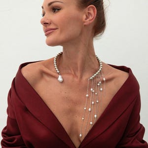 Peut inclure: Un collier imposant composé d'un épais tour de cou en perles métalliques rondes, d'un pendentif en perle baroque sur un côté et d'une frange en cascade de fines chaînes argentées ornées de petites perles blanches sur l'autre côté.