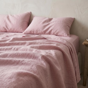 May include: A bed set featuring a pink and white striped pattern. The set includes two pillowcases and a fitted sheet, with the top sheet draped over the bed. The bedding has a soft, textured appearance.