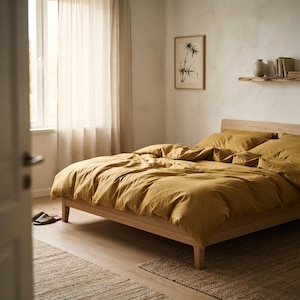 Pode incluir: Uma estrutura de cama de madeira com capa de edredão amarelo-mostarda e almofadas a condizer. A cama está posicionada num quarto com paredes claras, uma janela com cortinas transparentes, uma impressão de bambu e uma prateleira com livros.