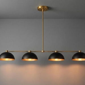 May include: A contemporary four-light pendant lamp with a brass finish and black dome shades. The interior of each shade is gold, reflecting the light. The fixture is suspended from the ceiling by a brass rod.