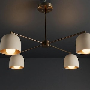May include: A contemporary ceiling light fixture featuring four cream-coloured, bell-shaped shades with gold interiors. Each shade houses a bright light. The fixture has a bronze finish and is mounted on a ceiling.