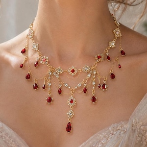 Peut inclure: Un collier doré orné de pierres précieuses rouges en forme de goutte et de cristaux transparents. Le collier présente un design délicat avec de multiples brins et pampilles, créant un look élégant et orné. Le collier est une pièce maîtresse.