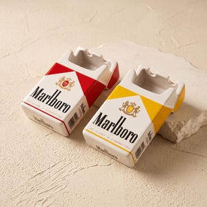 以下が含まれることがあります： タバコの箱の形をしたセラミック製灰皿2点。1点は赤と白のデザインで、Marlboro、20 Class A Cigarettesの文字と紋章が描かれています。もう1点は黄色と白のデザインで、同じ文字と紋章が描かれています。