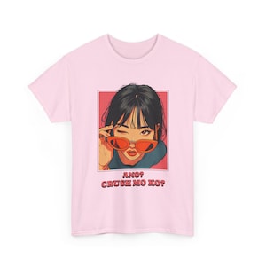 May include: A light pink t-shirt featuring a graphic of a woman winking while wearing orange sunglasses. The graphic is in a red rectangle with the text "ANO? CRUSH MO KO?" in a retro font.
