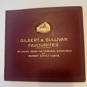 May include: A maroon-colored album with gold lettering that reads "GILBERT & SULLIVAN FAVOURITES." The album features the "His Master's Voice" logo and text indicating it was recorded under the supervision of Rupert D'Oyly Carte.