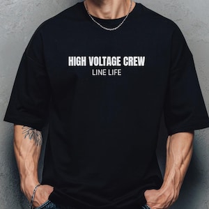 May include: Black oversized t-shirt with the text "HIGH VOLTAGE CREW LINE LIFE" in white. The shirt is paired with denim shorts. The model is standing in front of a gray wall.