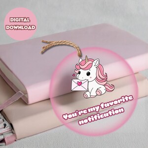 May include: A stack of two pink notebooks with a decorative pink circle featuring a cartoon unicorn holding a letter with a heart. The text "You're my favorite notification" is also on the circle. The words "DIGITAL DOWNLOAD" are in a pink circle.